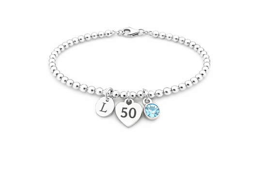Close-up of silver bracelet with dangling initial and sparkling birthstone for milestone birthday