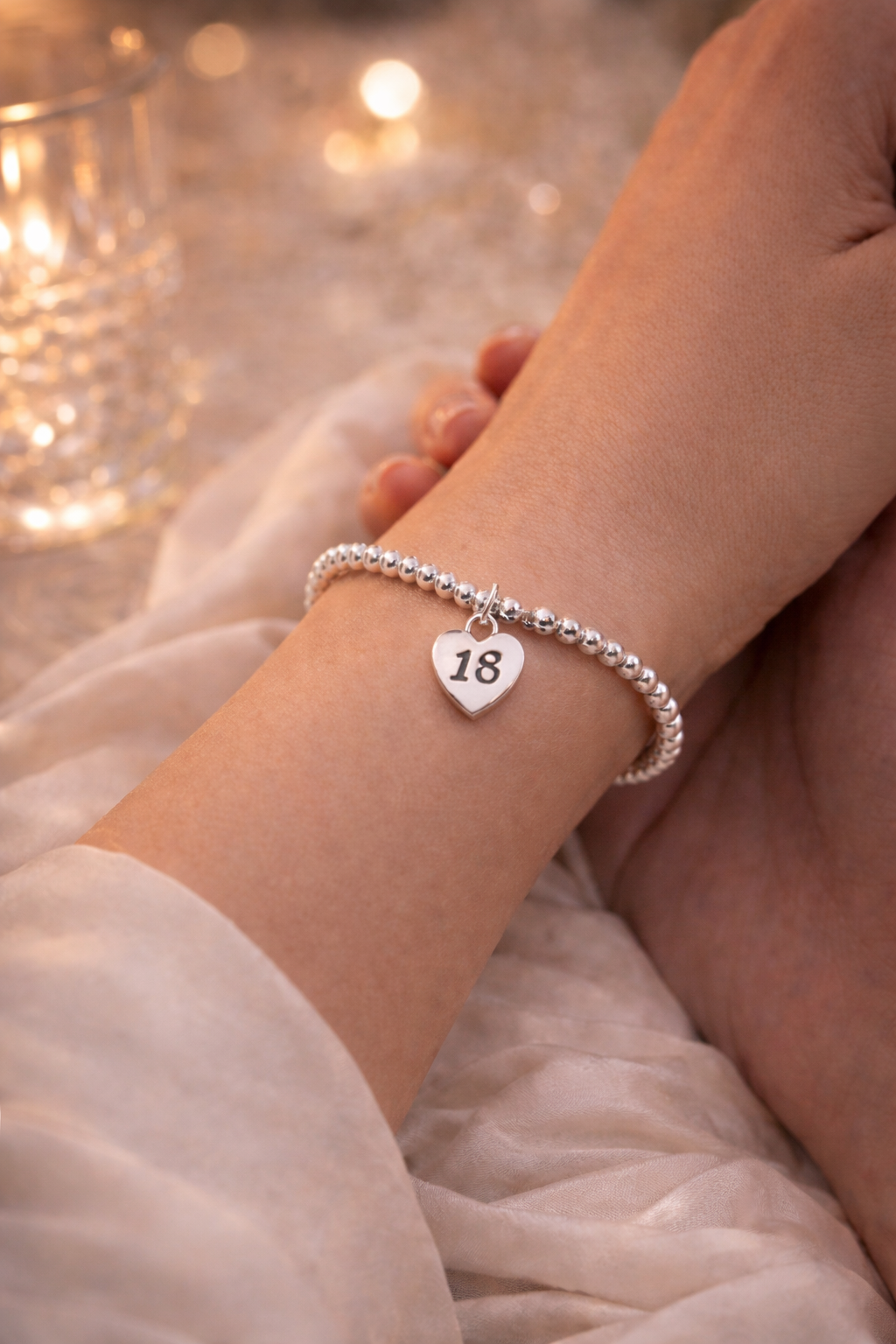 Close-up of silver bracelet with heart charm engraved 18