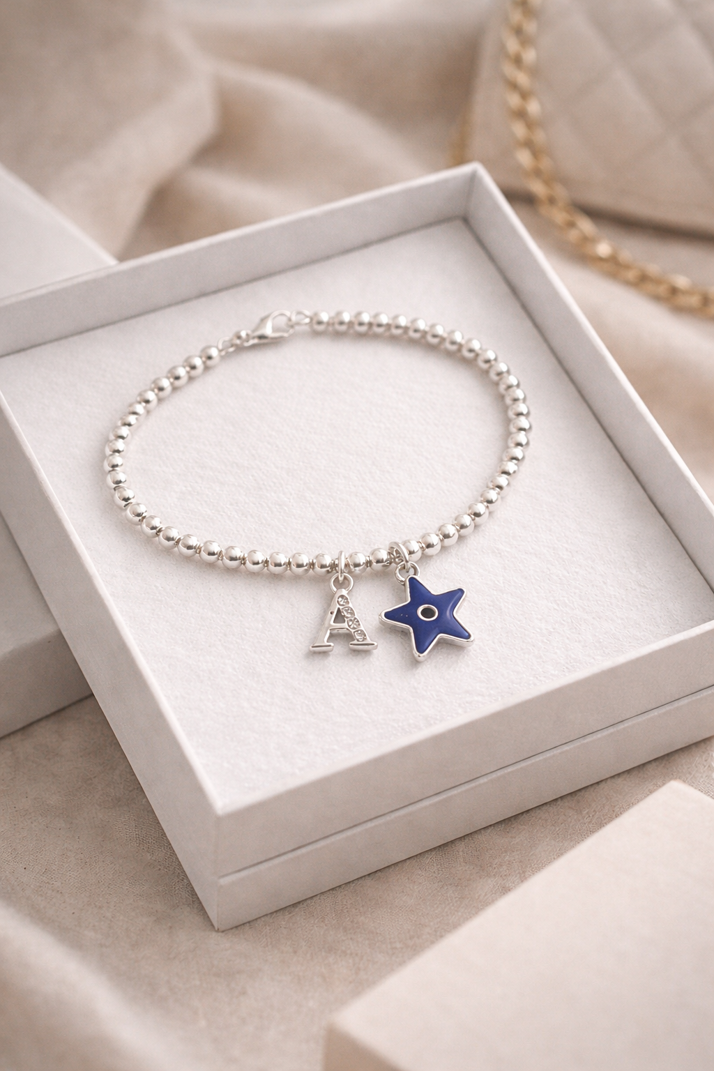 Silver bracelet with evil eye charm and letter 'A' charm in a white box.