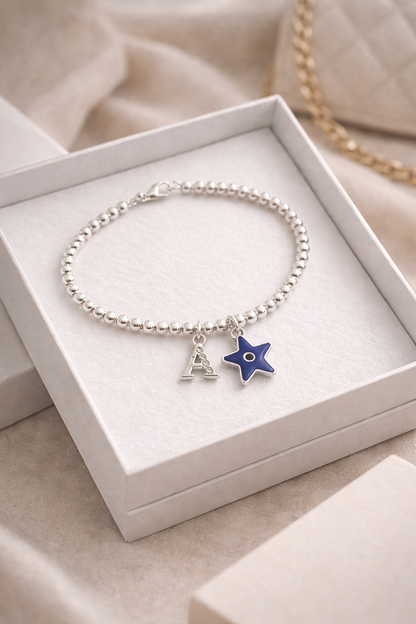 Silver bracelet with evil eye charm and letter 'A' charm in a white box.