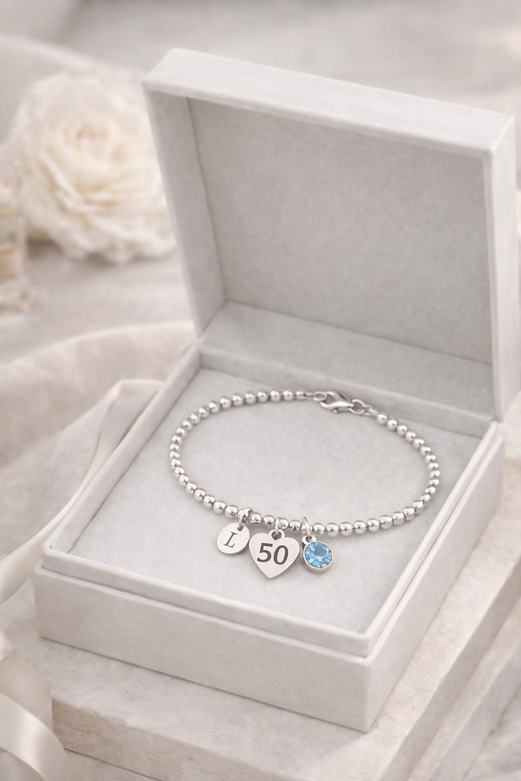 Silver bracelet with initial charm and birthstone, designed for a 50th birthday gift.