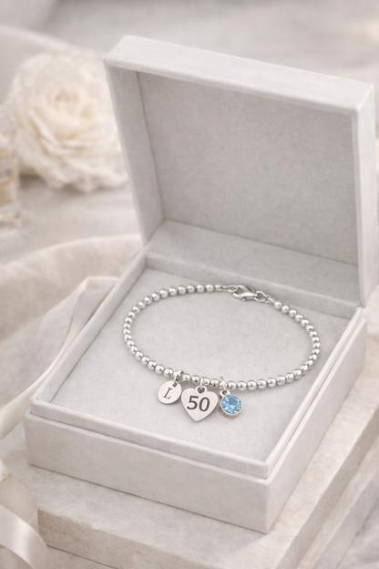 Silver bracelet with initial charm and birthstone, designed for a 50th birthday gift.